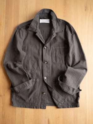 Mörk Oliv/Grå overshirt från A Day's March - Stilren mörkgrå overshirt / Chore Jacket från A Day's March i kraftig bomull. Klassisk krage, tre utanpåliggande fickor och knäppning framtill. Perfekt lager-på-lager-plagg med avslappnad passform och uppvikta ärmar för en casual look.