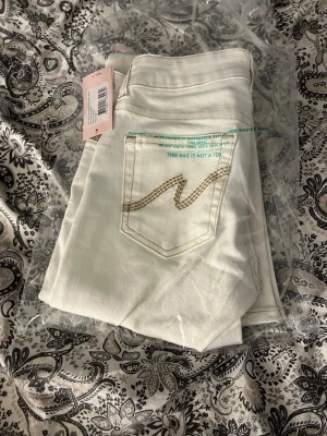Vita bootcut jeans från Nelly - Snygga vita bootcut jeans från Nelly med klassisk femficksdesign och beige broderad detalj på bakfickan. Jeansen har en rak passform upptill och utsvängda ben. Tillverkade i ett mjukt och stretchigt material för extra komfort.