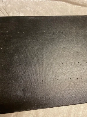 Svart canvas smyckensställ  - Säljer en svartmålad canvasduk med ett unikt hålmönster för örhängen och halsband . Duken är uppspänd på en träram och har små hål i raka linjer över hela ytan . Perfekt för DIY-projekt eller som dekoration.