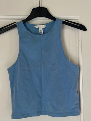 Blå croppad topp från H&M - Säljer en blå croppad topp från H&M. Tillverkad i mjuk bomullsmix som känns skön mot huden. Perfekt att matcha med jeans eller kjol.