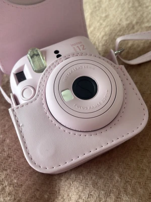 Rosa Fujifilm Instax Mini 12 kamera - Säljer en söt rosa Fujifilm Instax Mini 12 direktfilmskamera med matchande skyddsväska i konstläder. Kameran har en rund, kompakt form och är perfekt för att ta instantbilder. Väskan har axelrem och stängs med lock. Enkel att ta med överallt! Helt oanvänd. Pågrund av att jag har en Canon g7x mark iii. 