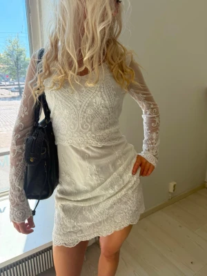 Vit spetsklänning med lång ärm - Söt vit kortklänning med långärmade spetsdetaljer och vackert broderat mönster. Klänningen har rund halsringning och figurnära passform. Perfekt för dig som vill ha en romantisk och elegant look.
