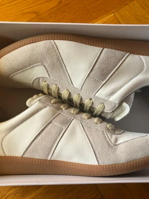 Maison margiela gats - Snygga Maison Margiela gats sneakers i beige och vitt med ovandel i mocka och läder. Klassisk gummisula och neutrala snören. Perfekta för dig som gillar märkeskläder, priset är svinbra pågrund av att de är köpta på Plick helt nya för 4000 och är lite osäker på äkthet och kan tyvärr inte garantera de. Det är oanvända men sen så köpte morsan ett par svarta som jag själv gillade mer så använde aldrig dessa, box ingår, skriv vid minsta fundering och fraktar vid samma dag  1599 superpris.