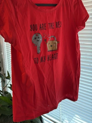 Röd t-shirt med gulligt tryck - Röd t-shirt från SisterS Point med ett gulligt tryck av ett hjärta, nyckel och lås samt texten 'You are the key to my heart'. T-shirten har rund halsringning och korta ärmar. Perfekt för dig som gillar söta motiv och färgglada plagg.