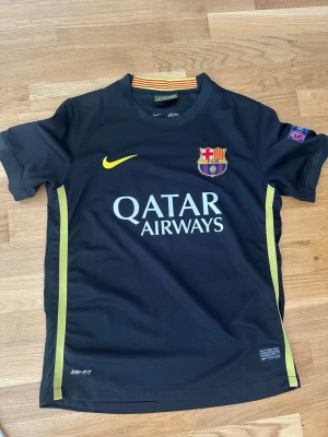 Barcelona Dani Alves matchtröja - Snygg svart Barcelona matchtröja från Nike med gula detaljer och tryck. På framsidan finns Qatar Airways-logga och klubbmärke, på baksidan står det Dani Alves och nummer 22 i gult. Tillverkad i Dri-FIT material som andas, perfekt för fotboll eller träning.