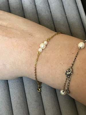 Guldfärgat armband med pärlor - Snyggt armband med tunn guldfärgad kedja och tre vita pärlor i mitten. Enkel och stilren design som passar till många olika looks. Justerbar längd med liten bricka vid låset.