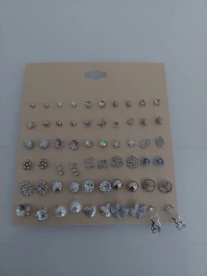 Set med 30 par silvriga örhängen - Säljer ett stort set med 30 par örhängen i olika former och stilar. Örhängena är silvriga och har detaljer som blommor, stjärnor, pärlor, fjärilar och glittrande stenar. Perfekt för dig som vill variera din look med många olika motiv och former.