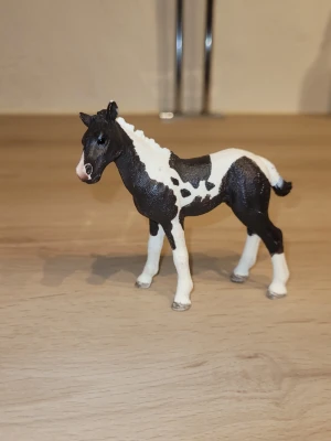 Svartvit hästfigur från Schleich - En detaljerad hästfigur i svart och vitt, från Schleich. Hästen har vita ben, svart kropp med vita fläckar och en vit man. Perfekt som prydnad eller leksak för samlare och hästälskare.