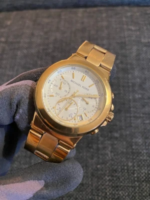 Michael Kors Watch Runway Chronograph, gold - Säljer en stilren och klassisk damklocka från Michael Kors, modell MK5222 i elegant guld ton. Klockan har en boett på 38 mm med kronograffunktioner (stoppur) och datumvisning.  Mycket gott skick överlag. Den är sparsamt använd och har naturligt slitage på länk. Ingenting nämnvärt och guldet är intakt. Se bilder för egen bedömning av det fina skicket. Klockarmbandet passar en handled på upp till ca 16 cm. Säljes ej funktionstestad då batteriet behöver bytas. 