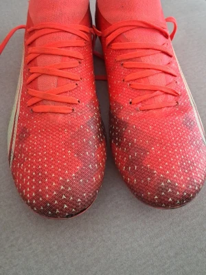 Röda Puma fotbollsskor med dobbar - Säljer ett par röda fotbollsskor från Puma med vita detaljer och klassisk logga på sidan. Skorna har snörning, stickad ovandel och fasta dobbar för bra grepp på planen. Perfekta för dig som vill sticka ut på matchen!