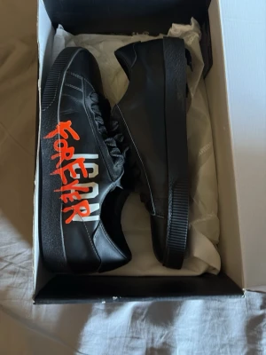Svarta Dsquared2 sneakers ICON FOREVER - Coola svarta sneakers från Dsquared2 med texten 'ICON FOREVER' i vitt och rött på sidan. Skorna har en låg profil och är tillverkade i läder med gummisula där Dsquared2-loggan syns. Perfekt för dig som vill sticka ut med ett unikt och trendigt par sneakers.