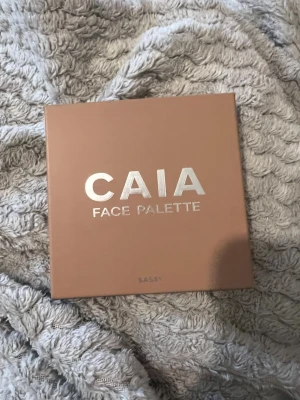 CAIA Face Palette Sassy bronzer - Snygg ansiktspalett från CAIA i färgen Sassy som är oanvänd, endast öppnat kartongen. Paletten innehåller fyra puder: en bronzer i varm brun nyans, en contour i kallare brun, en rosa blush och en skimrande highlighter. Kommer i en fyrkantig, beige förpackning med spegel i locket.
