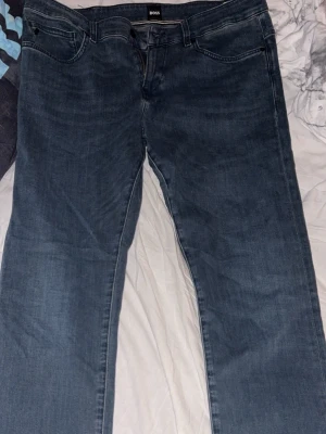 Blå jeans från BOSS  - Snygga blå jeans från BOSS, modell Delaware. Klassisk femficksdesign med raka ben och normal midja. Jeansen är tillverkade i denim och har subtila slitningar för en cool look. Perfekta för dig som gillar stilrena och tidlösa jeans.