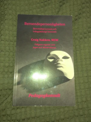 Beroendepersonligheten av Craig Nakken - Boken 'Beroendepersonligheten' av Craig Nakken utforskar beroendeprocessen och tvångsmässigt beteende. Omslaget är svart med en vit mask och rosa text. Perfekt för dig som vill förstå mer om beroende och dess påverkan på individ och familj.