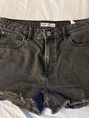 Grå jeansshorts från Bliss - Snygga grå jeansshorts från Cubus med råa, fransiga kanter och klassisk femficksdesign. Hög midjade, storlek 36 men sitter lite löst.