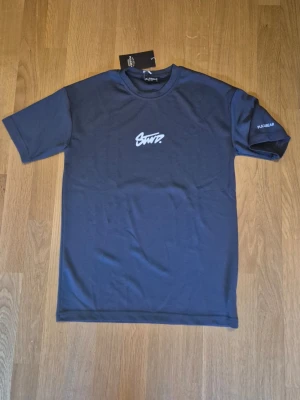 Mörkblå t-shirt från Pull&Bear - Snygg grå-mörkblå t-shirt från Pull&Bear med vit grafisk text på bröstet och logga på ärmen. Klassisk rund halsringning och korta ärmar. Tillverkad i mjukt bomullsmaterial som känns skönt mot huden. Perfekt för en avslappnad och trendig stil. Mer gråblå i färgen. Helt ny, oanvänd.
