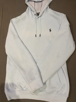 Babyblå hoodie från Polo Ralph Lauren - Babyblå hoodie från Polo Ralph Lauren. Riktigt skön och mjuk, även fickor där fram. Väldigt clean och enkel, passar till allt. Helt ny, ej använd.