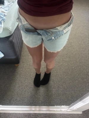 Ljusblå denimshorts med fransad kant - Säljer ett par ljusblå denimshorts med fransad kant och klassiska bakfickor. Shortsen har en hög midja och är tillverkade i bomull, perfekta för varma dagar. Snygg och avslappnad passform som passar till det mesta.
