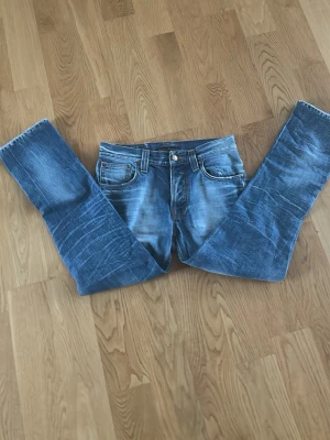 Blå raka jeans med slitningar - Snygga blå jeans med raka ben och coola slitningar framtill och baktill. Klassisk femficksmodell med knapp- och dragkedjegylf. Jeansen har en tvättad look och kontrastsömmar. Perfekta för en avslappnad streetstil.