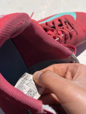 Röda Nike Mercurial fotbollsskor - Säljer ett par röda Nike Mercurial fotbollsskor med turkosa detaljer och snörning. Skorna har en låg profil och är tillverkade i syntetmaterial för bra bollkontroll. Perfekta för dig som vill sticka ut på planen med stilrena och sportiga skor.
