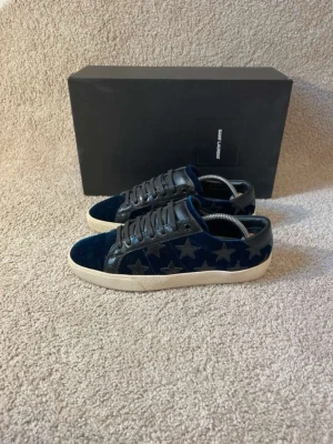 Saint Laurent blå sammetssneakers - Unika sneakers från Saint Laurent i blå sammet med stjärnmönster på sidorna och svarta läderdetaljer. Skorna har vita sulor och svarta skosnören. Perfekta för dig som vill sticka ut med en lyxig och cool stil.