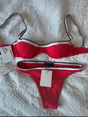 Röd bikini med kontrastkant från ZARA - Oanvänd med lapp kvar! Snygg röd bikini från ZARA med vita och svarta kontrastkanter. Överdelen har bygel och reglerbara axelband, medan underdelen har samma dekorativa kant. Perfekt för stranden eller poolen.