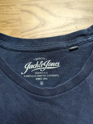 Blå Jack & Jones t-shirt med tryck - Snygg mörkblå t-shirt från Jack & Jones med stort vitt tryck på bröstet. Klassisk rund halsringning och korta ärmar. Perfekt för en avslappnad och cool stil.