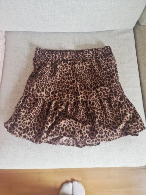 Leopardmönstrad volangkjol - Snygg kort kjol med leopardmönster och volang. Kjolen har resår i midjan och är perfekt för dig som vill sticka ut med en trendig look. Materialet känns mjukt och lätt, vilket gör den bekväm att bära hela dagen.