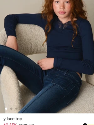 Mörkblå långärmad topp med spets - Mörkblå långärmad topp med smal passform och v-ringning dekorerad med spetsdetalj vid halsen. Perfekt att styla med jeans för en snygg och enkel look.