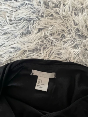 Svart one shoulder klänning H&M - Aldrig använd. Snygg svart one shoulder klänning från H&M i stretchigt material. Klänningen har draperad effekt längs sidorna och en asymmetrisk axel, vilket ger en trendig och stilren look.