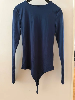 Mörkblå långärmad body - Snygg mörkblå långärmad body med rund halsringning. Tight passform och tillverkad i ett stretchigt material som känns bekvämt mot huden. Perfekt att styla med jeans eller kjol för en clean look. Har aldrig använt