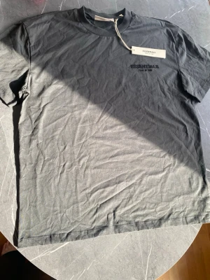 Essentials Fear Of God T-shirt svart – M - Säljer en svart Essentials Fear Of God T-shirt i mycket snygg modell. Minimalistisk design med Essentials-logo på bröstet och originaltag kvar.  * Färg: Svart * Storlek M * Essentials Fear Of God logo * Tag kvar * Bra skick  Perfekt basic/streetwear-plagg som passar till allt.