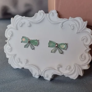 Mint Bow Earrings  - En tidlös elegans örhängen förenar en klassisk vintage-look med modern minimalism. Örhängen är prydda med ljusreflekterande kristaller i en förtrollande havsgrön nyans. Tillverkad i Korea.     Material: Rhodium , CZ-diamant Nickeltestat & allergivänligt                  Storlek: Längd ca 1,3cm Bredd ca 0.3cm -Inga prisförslag, tack.                                       - Varan packas noggrant och säkert 
