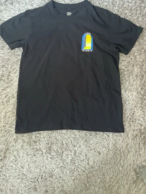 Svart Casa Blanca t-shirt med tryck - Svart t-shirt från Casa Blanca med färgglatt grafiskt tryck i blått, gult och grått på både bröstet och ryggen. Klassisk passform och rund halsringning. Perfekt för dig som gillar streetwear och snygga prints.