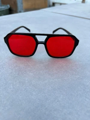 Svarta solglasögon med röda glas - Coola solglasögon med svart ram och röda fyrkantiga glas. Ramen har en unik design med dubbla bryggor och markerade kanter. Perfekta för dig som vill sticka ut med en retroinspirerad look. Helt perfekta och unika till en varm sommardag ⛱️🍉