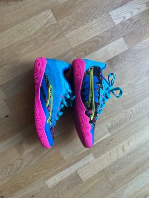 Färgglada sneakers från Puma - Säljer ett par unika sneakers från Puma med coolt mönster i blått, rosa och gult. Skorna har snörning och en vågig sula i rosa. Perfekta för dig som vill sticka ut med din stil!