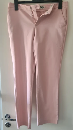 Ljusrosa kostymbyxor Twist & Tango - Ljusrosa lowrise kostymbyxor från Twist & Tango med raka ben och diskreta fickor fram och bak. Saknar en knapp på insidan men i övrigt fint skick.