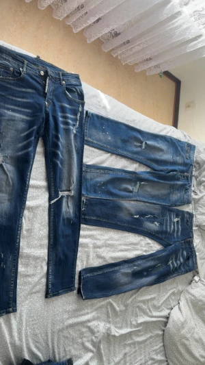 Blå slitna jeans från Dsquared2 - Säljer ett par blå jeans från Dsquared2 med slitningar, hål och distressed detaljer. Jeansen har smal passform, klassisk femficksdesign och tydliga tvättade partier för en cool, använd look. Perfekta för dig som gillar streetwear och trendig stil.