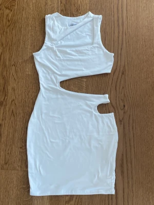Vit cut-out klänning från Fashion Nova - Trendig vit kortklänning från Fashion Nova med asymmetriska cut-out-detaljer i midjan. Klänningen är ärmlös och har en kroppsnära passform. Tillverkad i mjukt material som känns skönt mot huden.