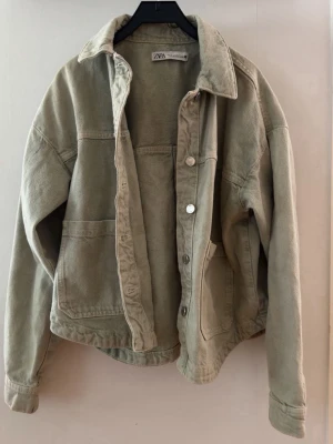 Grön jeansjacka från ZARA - Snygg grön jeansjacka från ZARA med klassisk krage, stora framfickor och knäppning framtill. Jackan har en bra passform och är tillverkad i mjukt jeanstyg. Perfekt för sommaren