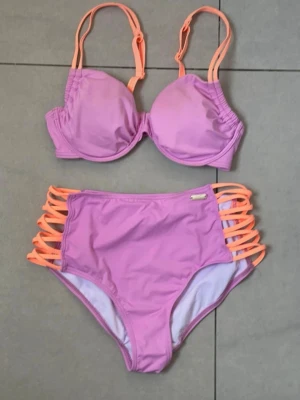 Rosa bikini med orange detaljer Venice Beach i storlek 36 i nyskick - Snygg bikini från Venice Beach i nyskick i rosa med orange snörningsdetaljer på sidorna av bikinitrosan. Storlek 36. Bh:n har justerbara axelband och vadderade kupor. Perfekt för sommarens strandhäng och poolpartyn.