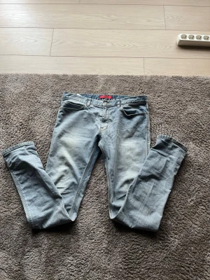 Ljusblå Hugo Boss slim fit jeans - Säljer ett par ljusblå Hugo Bodd slim fit jeans med klassisk femficksdesign och diskreta slitningar framtill. Jeansen har normal midja och raka ben. Perfekta för en avslappnad och trendig look. 33/34