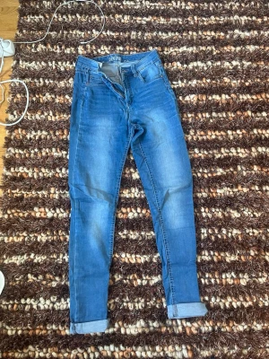 Kappahl - Blå slim fit jeans från Denim - Snygga blå slim fit jeans från Denim med klassisk femficksdesign och uppvikta benslut. Jeansen har en lätt tvättad look och normalhög midja. Perfekta för en avslappnad och trendig stil.