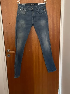 Blå jeans från Replay - Snygga blå skinny jeans från Replay med klassisk femficksdesign och dragkedjedetalj vid fickan. Jeansen har en lätt tvättad look med slitningar på låren och smal passform som sitter tajt hela vägen ner.