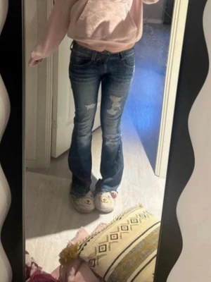 Blå bootcut jeans med slitningar - Säljer ett par blå bootcut jeans med slitna detaljer på låren och knäna. Jeansen har en klassisk femficksmodell och är tillverkade i denim med lätt stretch. Perfekta för en avslappnad och trendig look. jag har sytt de bootcut ifrån skinny! Måtten finns på bilderna