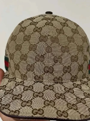 Beige keps från Gucci med GG-mönster - Säljer en beige keps från Gucci med det klassiska GG-monogrammet över hela kepsen. På sidan finns en grön och röd rand som ger extra lyxig känsla. Kepsen är tillverkad i canvasmaterial och har en böjd skärm.