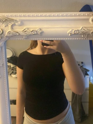 Svart topp med öppen rygg - Säljer en svart, tight topp med korta ärmar och öppen rygg. Toppen har en enkel och sopren design som sitter figurnära och är perfekt för dig som gillar minimalistisk stil. Materialet känns mjukt och stretchigt, troligen bomull eller polyester. Jag säljer den här för att den tyvärr är för liten för mig