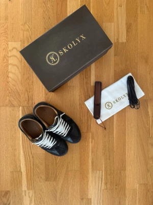 Skolyx GATS - Stilrena Mörkblåa sneakers från Skolyx med beige skosnören och detaljer i mocka och läder. Klassisk låg modell med bruna innersulor och diskret branding på insidan. Perfekta för dig som gillar en clean och tidlös look.