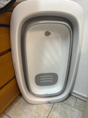 Vikbart badkar från Twistershake  - Säljer ett vitt och grått vikbart badkar från TINOSAFE. Badkaret är tillverkat i plast och silikon, perfekt för mindre utrymmen eller för dig som vill ha ett portabelt badkar. Smidig att fälla ihop och förvara när det inte används.