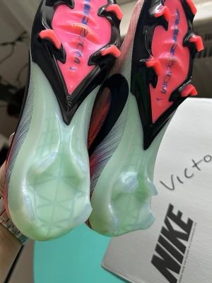 Nike Mercurial Vapor 16 Elite FG - Säljer ett par Nike Mercurial Vapor 16 Elite FG fotbollsskor i färgen Silt Red/Racer Blue. Skorna har en snygg rosa och blå gradient med svart Nike-swoosh och är tillverkade i lätt syntetmaterial för bästa känsla och grepp på planen.